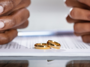 two hands from both sides of a table on top of divorce paperwork and two wedding rings