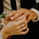 A couples hands putting on wedding rings.