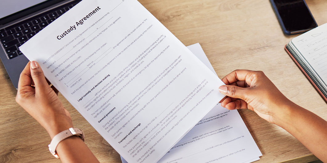 adult holding custody agreement paper over a laptop